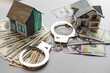 handcuffs, dollars, house figure on wooden background. violation of law. real estate fraud.