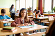 © Drazen - Happy schoolgirl during class in classroom looking at camera.