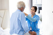 Asian female caregiver helping senior caucasian male dress up at home care. Professional caregiver nursing home