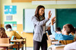 © Drazen - Happy elementary school teacher gives high-five to her student during class in classroom.