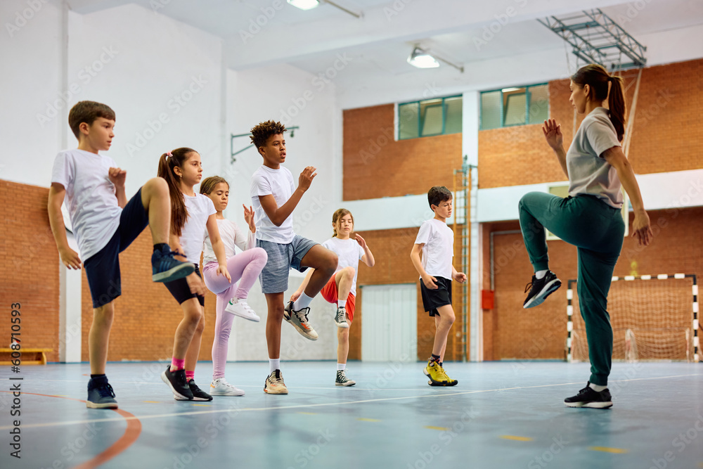 School kids and sports teacher exercising during PE class at school gym ...