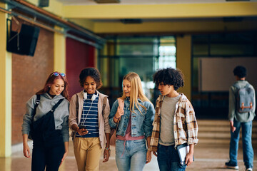 Wall Mural - Group of high school friends using cell phone while walking through hallway.