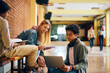 © Drazen - Black teenager using laptop while studying with his friends in high school hallway.