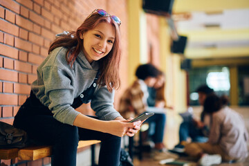 Wall Mural - Happy high school student text messaging on cell phone and looking at camera.