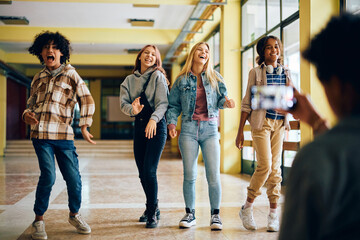 Wall Mural - Cheerful high school students goof around while friend is filming them with phone.