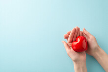 First Person Top View Photo Of Female Hands Cradling A Red Heart On A Pastel Blue Background. There's Empty Space For Text Or An Ad. It's A Concept For World Blood Donor Day
