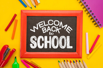 Back to school written in chalk on a framed blackboard. Top view flat lay concept. Lettering on chalkboard for high school, secondary school, grammar schools, colored paper, supplies, stationery