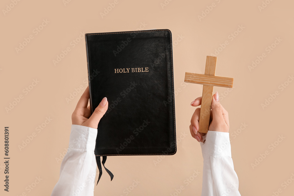 Female hands with Holy Bible and cross on pale orange background