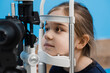 Ophthalmologist illuminates eye of child with light from slit lamp to diagnose the eyes and cornea. Pediatric ophthalmologist with slit lamp examines eyes and cornea of child.