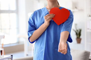 Female nurse with paper heart in clinic, closeup