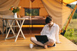 © Ananass - Pretty woman using cellphones and notebook sitting in tent during camping on summer day