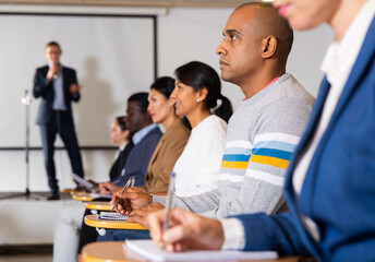 Wall Mural - Concentrated Hispanic man sitting in conference room listening to lecturer and making notes during business training