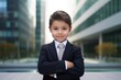 Portrait of a cute little boy in a business suit on the background of a modern building