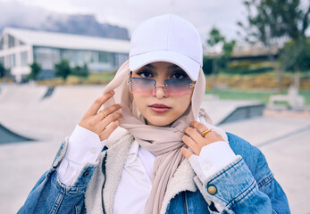 Portrait, fashion or sunglasses with an islam woman outdoor in a cap and scarf for contemporary style. Arab, face and hijab with a trendy young muslim female person posing outside in modern eyewear