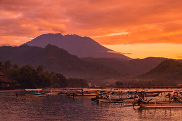 Wall Mural - Colorful sunset or sunrise with scenic landscape with volcano and quiet ocean with fishing boats
