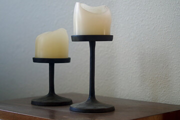 two cream white decorative candles in simple, functional  metal candle holders on a dark wood table