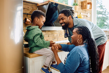 Wall Mural - Happy black parents talk to their small son in kitchen.