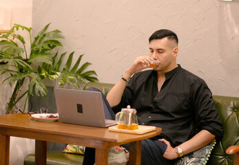 Handsome male freelancer enjoys working on laptop and thinking of new ideas while drinking morning tea in cafe  