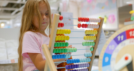 Little girl pupil hand counts moving small beads on colorful toy abacus.
