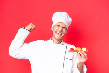 Wall Mural - Young caucasian chef man holding sashimi isolated on red background celebrating a victory