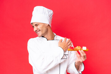 Wall Mural - Young caucasian chef man holding sashimi isolated on red background suffering from pain in shoulder for having made an effort