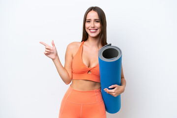 Wall Mural - Young beautiful sport woman going to yoga classes while holding a mat isolated on white background pointing finger to the side