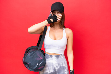 Wall Mural - Young beautiful sport woman with sport bag isolated on red background covering eyes by hands. Do not want to see something