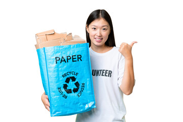 Wall Mural - Young Asian woman holding a recycling bag full of paper to recycle over isolated chroma key background pointing to the side to present a product