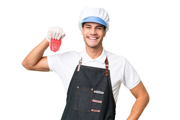 Wall Mural - Butcher caucasian man wearing an apron and serving fresh cut meat over isolated background posing with arms at hip and smiling