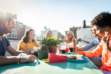 Multiethnic group of young happy friends bonding and having party at home on a rooftop terrace with New York city view