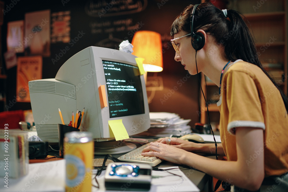 Young woman in headphones typing codes for new software on computer ...
