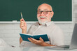 © Volodymyr - Smiling senior teachers teaching in the classroom on chalkboard. Teacher at university. Portrait of mature teacher professor at table in school. Senior teacher. Mature teacher. Professor on blackboard