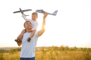 cute little boy and his handsome young dad are smiling while playing with a toy airplane in the park