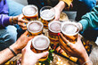 Multiracial group of young people cheering glass of beer together at brewery pub- Happy friends enjoying summer drinking blonde pint sitting at bar table- Food and beverage concept-Youth culture 