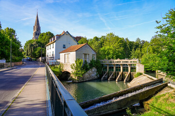 Wall Mural - Dam on the Grand Morin river next to a tannery containing a watermill, bypassed by a concrete fish ladder, in front of the Church of Saint Denys and Saint Foy in Coulommiers, Seine et Marne, France