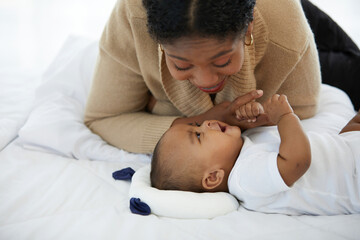 Wall Mural - African young mother playing with her adorable baby on bed