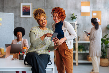 Two multiracial female colleagues using phone in office.