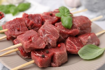 Wall Mural - Wooden skewers with cut fresh beef meat, basil leaves and spices on beige plate, closeup