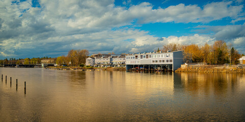 Wall Mural - Magog city skyline and marina landscape in the bay next to Ponte-Merry Park in Quebec, Canada, golden reflections on the water and dramatic cloudscape