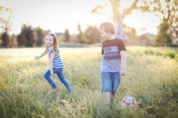 Wall Mural - Boy and girl running through long grass playing soccer at the park. Aussie kids having fun outdoors in nature