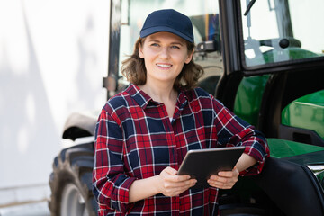 Sticker - Woman farmer with a digital tablet on the background of an agricultural tractor	