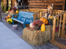 A Blue Bench Sits Outside A Wooden Barn Adorned With Fall Accessories Such As Pumpkins, Mums Flowers And Hay.