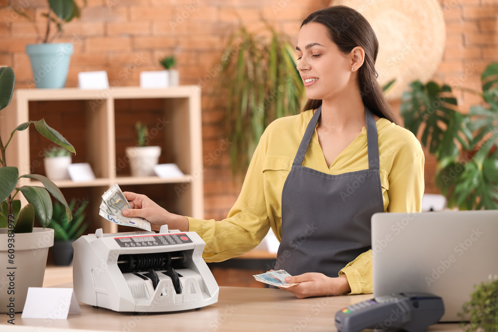 Female cashier using cash counting machine in flower shop