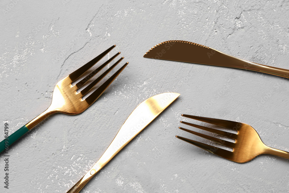 Golden forks and knives with green handles on grey background
