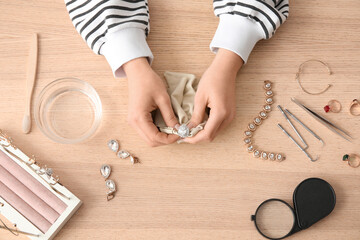 Woman cleaning beautiful jewelry at wooden table