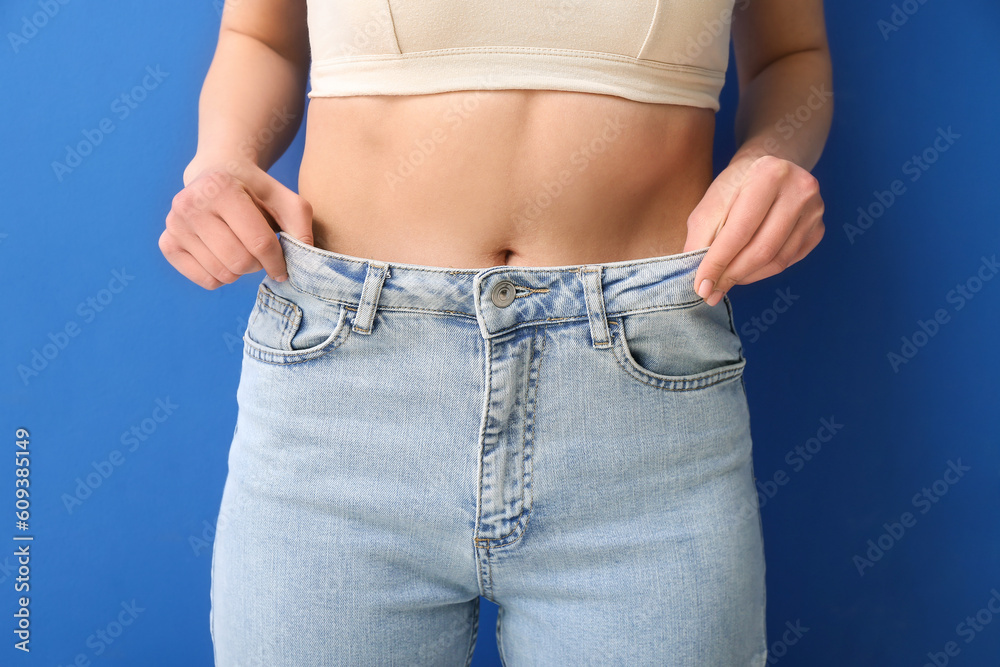 Young woman in loose jeans on blue background. Diet concept