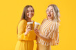 © Pixel-Shot - Young sisters with cups of coffee on yellow background
