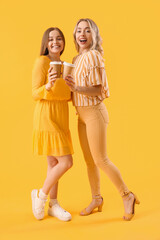 Poster - Young sisters with cups of coffee on yellow background