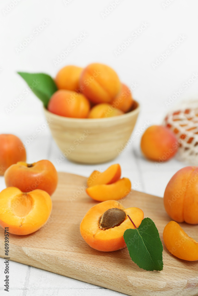 Board and bowl with fresh apricots on white tile table