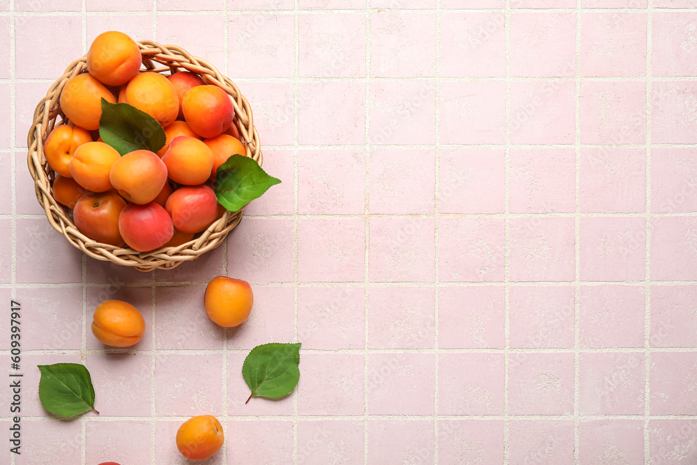 Wicker bowl with fresh apricots on pink tile background